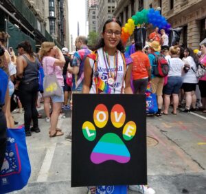 person at NYC world pride parade holding LOVE paw print sign in pride colors